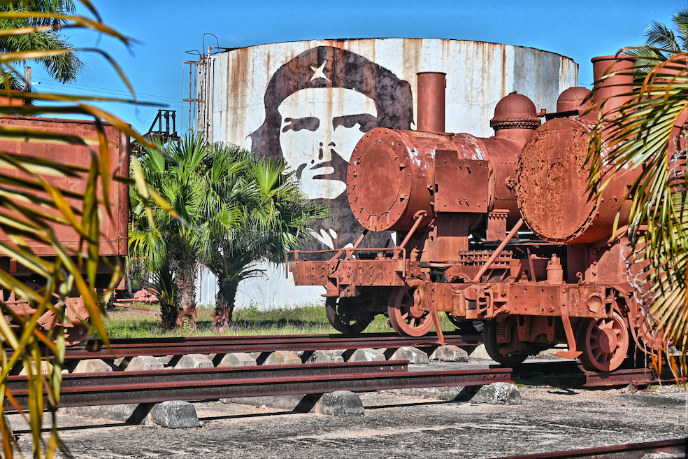 Rusting Cuban train beside a Che Guevara mural and palm trees
